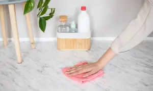 Hand wiping a marble floor with a pink cloth, with cleaning supplies in the background.