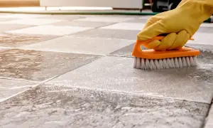 A gloved hand scrubs a tiled floor with a brush, showing the best way to clean porcelain tile.