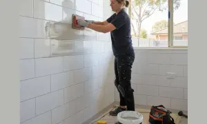 A woman is re grouting a white tiled wall with a trowel.