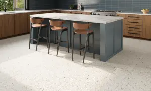 A modern kitchen with a blue island, wooden cabinets, and a beautiful bella terrazzo floor. Three bar stools are pulled up to the island.