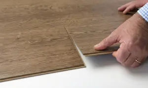 Hands demonstrate how to replace vinyl plank flooring by clicking a new plank into place.