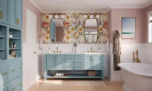A bright bathroom with a floral wallpaper, a blue double vanity, and a freestanding tub. This blue is a beautiful choice for the best color for bathroom cabinets.