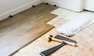 Tools for installing LVT flooring, including a rubber mallet and pry bar, are laid out next to planks being fitted.