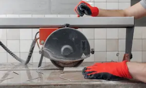 Hands in red gloves guide a tile on a wet saw, demonstrating how to use a wet saw for precise cuts.