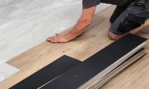 A person is installing vinyl plank flooring, carefully laying down a plank on a prepared surface.