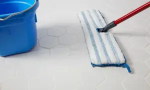 A blue bucket and a mop are used to clean white hexagonal porcelain tile floors.