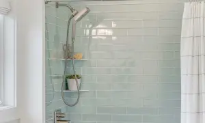 Modern shower with light blue subway tiles. A shower head and hose hang next to a small plant. This is the best way to regrout tiles for a fresh look.