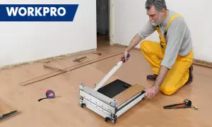 Man in yellow overalls uses a WORKPRO flooring cutter to demonstrate how to cut flooring. Tools and planks are nearby.