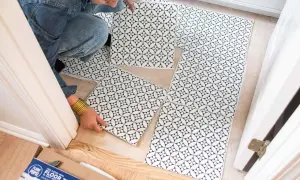 A person is laying down black and white patterned peel and stick floor tiles. No grout is needed for these tiles.