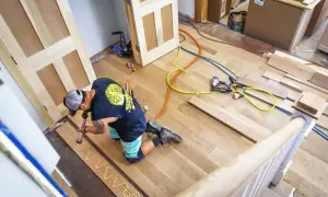A worker applies adhesive to planks, demonstrating how to install luxury vinyl tile. Tools and materials are nearby.