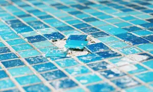 Close-up of a damaged mosaic tile surface, showing loose blue glass tiles. This image highlights the need to install glass mosaic tiles carefully.
