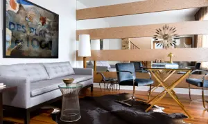 A large wall mirror with wood accents offers a stylish way to decorate around it. A grey sofa, abstract art, and a glass desk complete the modern living space.