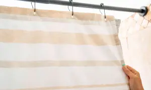 A hand holds a striped shower curtain hanging from a rod.