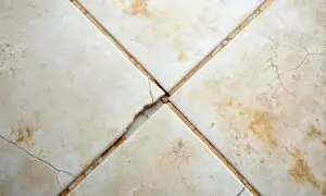 Cracked grout between beige floor tiles. Consider how often should you regrout floor tiles to prevent this damage and maintain your floor's integrity.