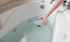 A hand pours liquid from a glass into a jetted bathtub, part of a process for how to clean bathtub.
