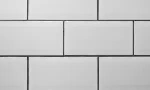 A clean, modern wall features rows of white tile with thin, dark grey grout lines, creating a classic subway tile pattern.