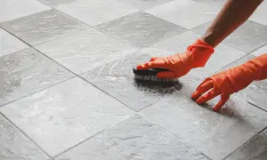 Hands in orange gloves scrub a tiled floor. The person is working to polish porcelain tile, making it shine.