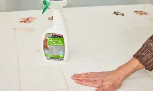 A hand wipes a stained porcelain floor tile with Bona Hard-Surface Floor Cleaner, showcasing effective porcelain floor tile cleaners.