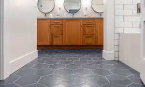 Hexagonal floor tiles create a dynamic pattern, giving the illusion of a larger space. A wooden vanity with three circular mirrors sits above.
