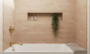 A modern bathroom with a random subway tile pattern in a warm, peachy hue. A gold faucet and shower controls complement the tiles.