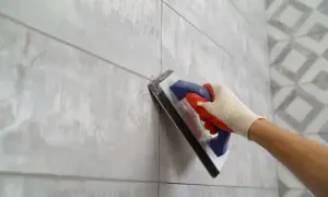 Gloved hand applies grout to a tiled wall, ensuring the best grout for shower floor longevity.