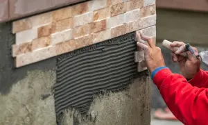 Hands expertly apply stone tile to a wall, demonstrating how to install stone tile on wall with notched trowel and adhesive.