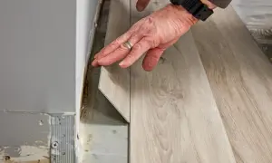 Hands installing light wood-look vinyl plank flooring. The question of how long does it take to install vinyl plank flooring depends on room size and prep.