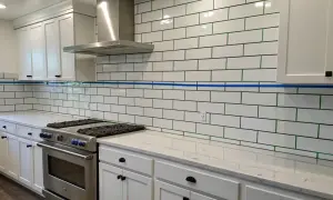 A kitchen backsplash features white subway tile with striking green grout, a modern contrast to the white cabinets and stainless steel appliances.