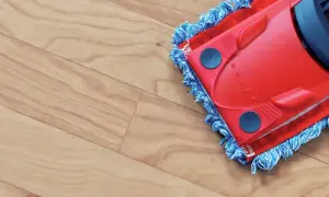 A red mop with blue fringe is cleaning a light wood-look vinyl floor, leaving it spotless.