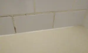 Cracked grout lines between light grey tiles suggest a need for repair. The question is, can you grout over grout?