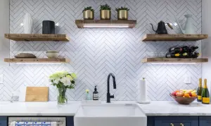 A modern kitchen with a white chevron tile backsplash, rustic wood shelves, and a farmhouse sink. The chevron tile out of style? Not in this chic design!