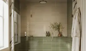 A modern shower with two-toned, low maintenance shower tile in beige and sage green. A glass enclosure, rainfall showerhead, and a plush robe complete the serene space.
