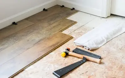 Tools for installing LVT flooring, including a rubber mallet and pry bar, are laid out next to planks being fitted.