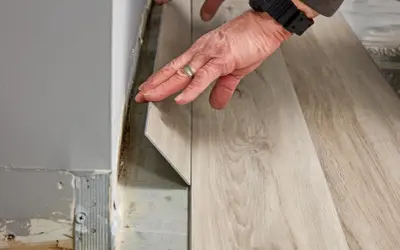 Hands installing light wood-look vinyl plank flooring. The question of how long does it take to install vinyl plank flooring depends on room size and prep.