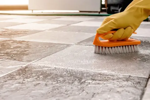 A gloved hand scrubs a tiled floor with a brush, showing the best way to clean porcelain tile.