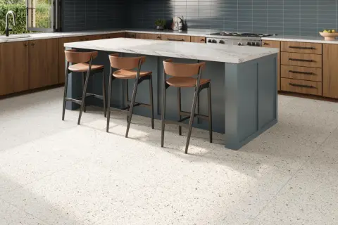 A modern kitchen with a blue island, wooden cabinets, and a beautiful bella terrazzo floor. Three bar stools are pulled up to the island.