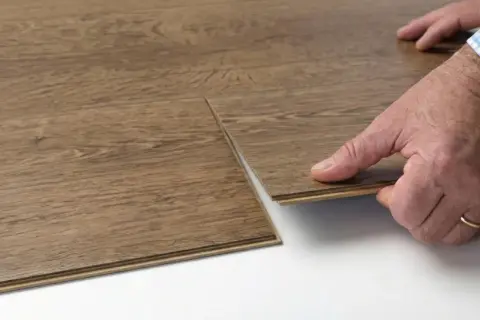 Hands demonstrate how to replace vinyl plank flooring by clicking a new plank into place.