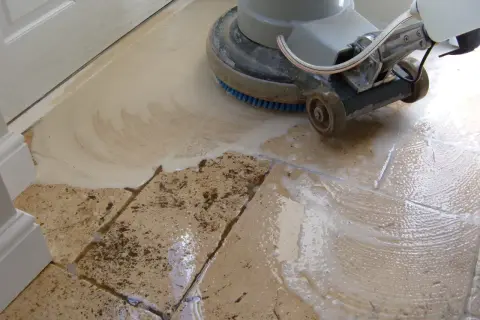 A floor buffer machine is used to clean travertine tile, creating suds and removing dirt.