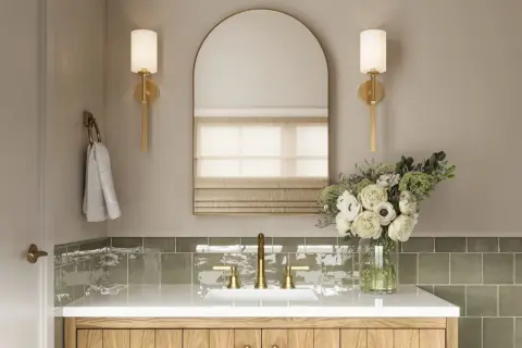 Elegant bathroom vanity with brass fixtures, a large arched mirror, and wall sconces that cast light up and down. A bouquet of white flowers adds a touch of luxury.