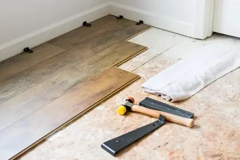 Tools for installing LVT flooring, including a rubber mallet and pry bar, are laid out next to planks being fitted.