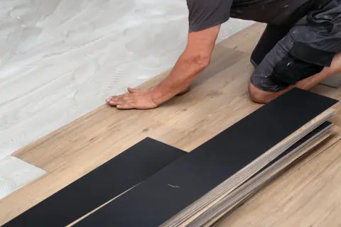 A person is installing vinyl plank flooring, carefully laying down a plank on a prepared surface.
