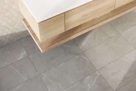 A modern bathroom vanity with wood grain drawers sits above large format tile flooring. The grout lines are thin, emphasizing the size of the tiles.