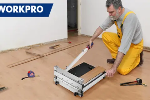 Man in yellow overalls uses a WORKPRO flooring cutter to demonstrate how to cut flooring. Tools and planks are nearby.