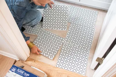 A person is laying down black and white patterned peel and stick floor tiles. No grout is needed for these tiles.