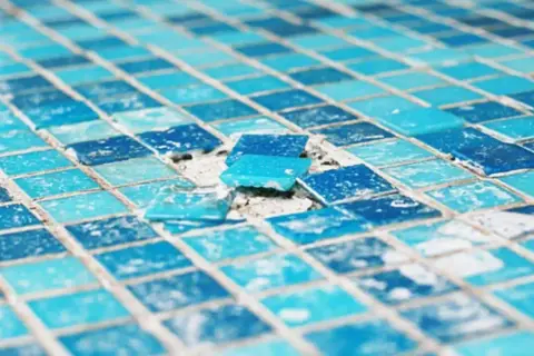 Close-up of a damaged mosaic tile surface, showing loose blue glass tiles. This image highlights the need to install glass mosaic tiles carefully.