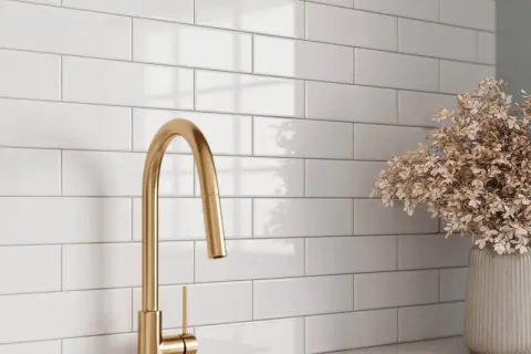 A gold faucet and dried flowers complement a white subway tile backsplash, showcasing a clean look after learning how to grout subway tile.