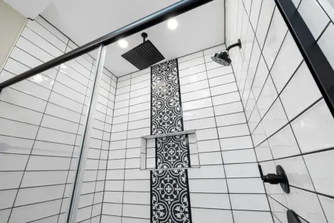 Modern shower with white subway tiles and black grout, featuring a decorative black tile accent and black fixtures.