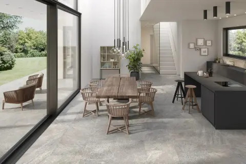 Modern dining and kitchen area with a seamless stone flooring installation, connecting indoor and outdoor spaces.