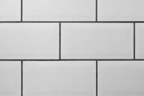 A clean, modern wall features rows of white tile with thin, dark grey grout lines, creating a classic subway tile pattern.