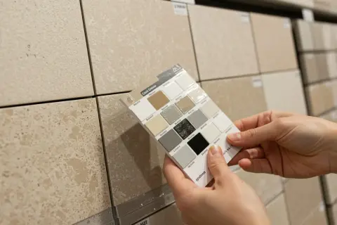 Hands hold a grout color swatch against beige tiles, exploring options for the best grout color for beige tile.